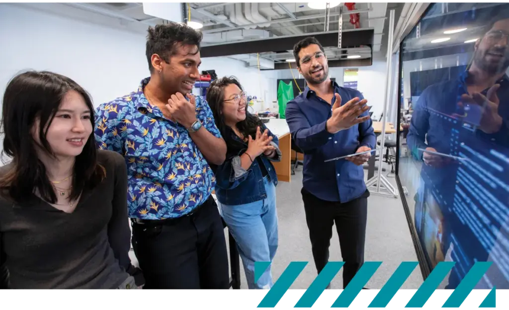 Four people examine a large monitor displaying code in a modern workspace.